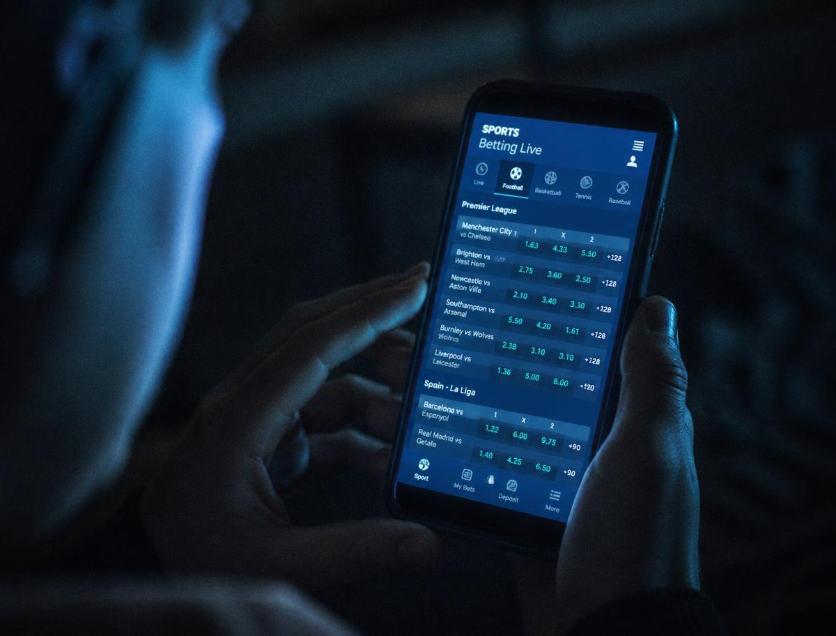Manos sosteniendo un teléfono con una aplicación de apuestas deportivas de noche